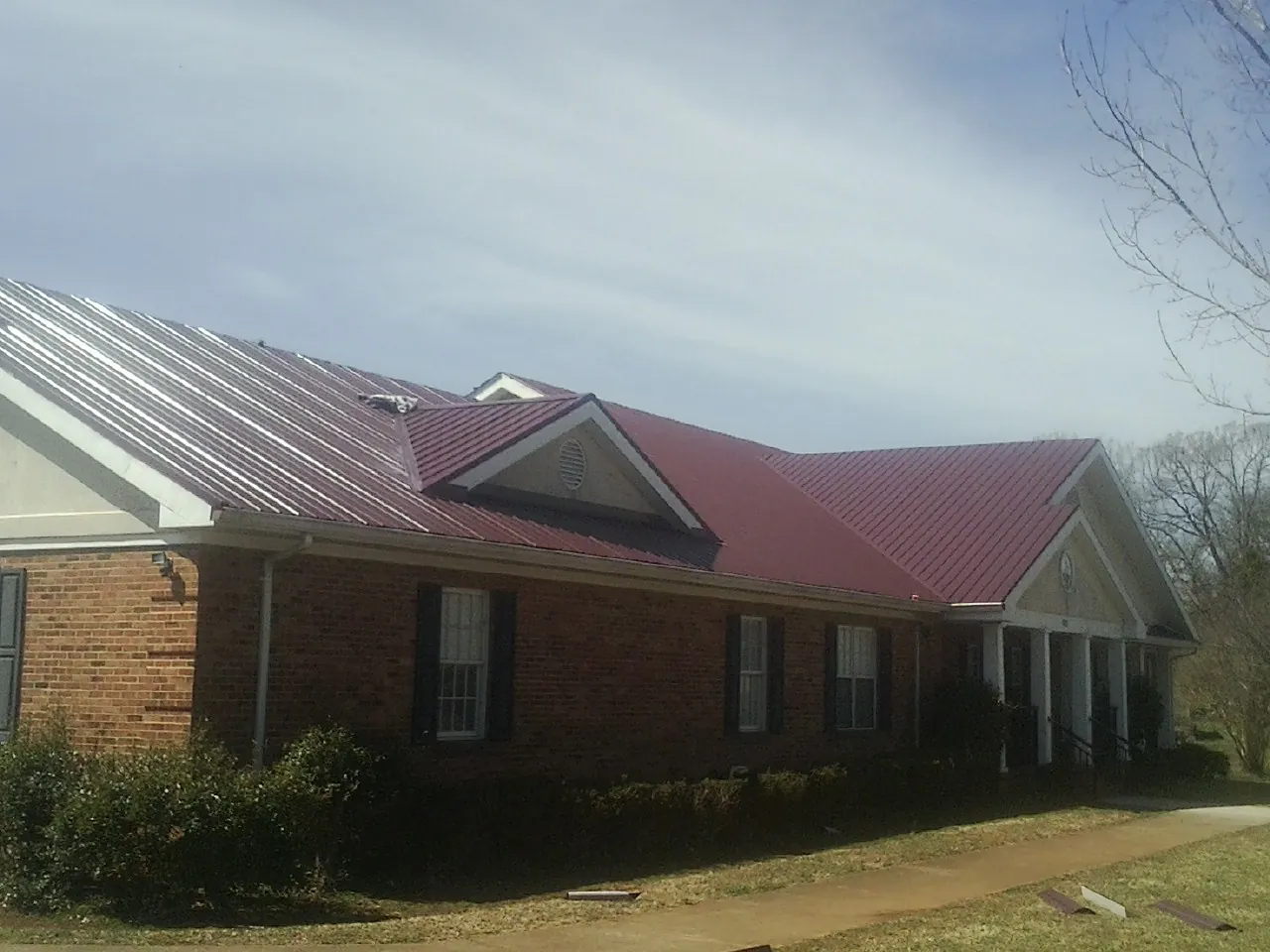 Red metal roof with gabled entries on a long brick building, from a Hail Damage Roof Repair job in Robbins