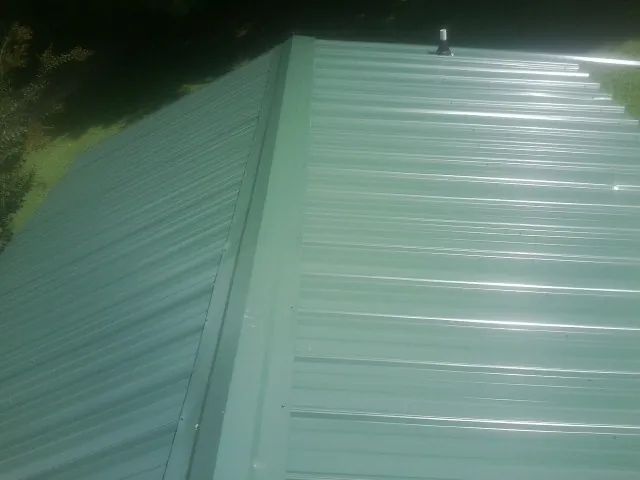 New green metal panels meeting at the ridge of a roof — Flat Roof Repair work by our crew in Robbins