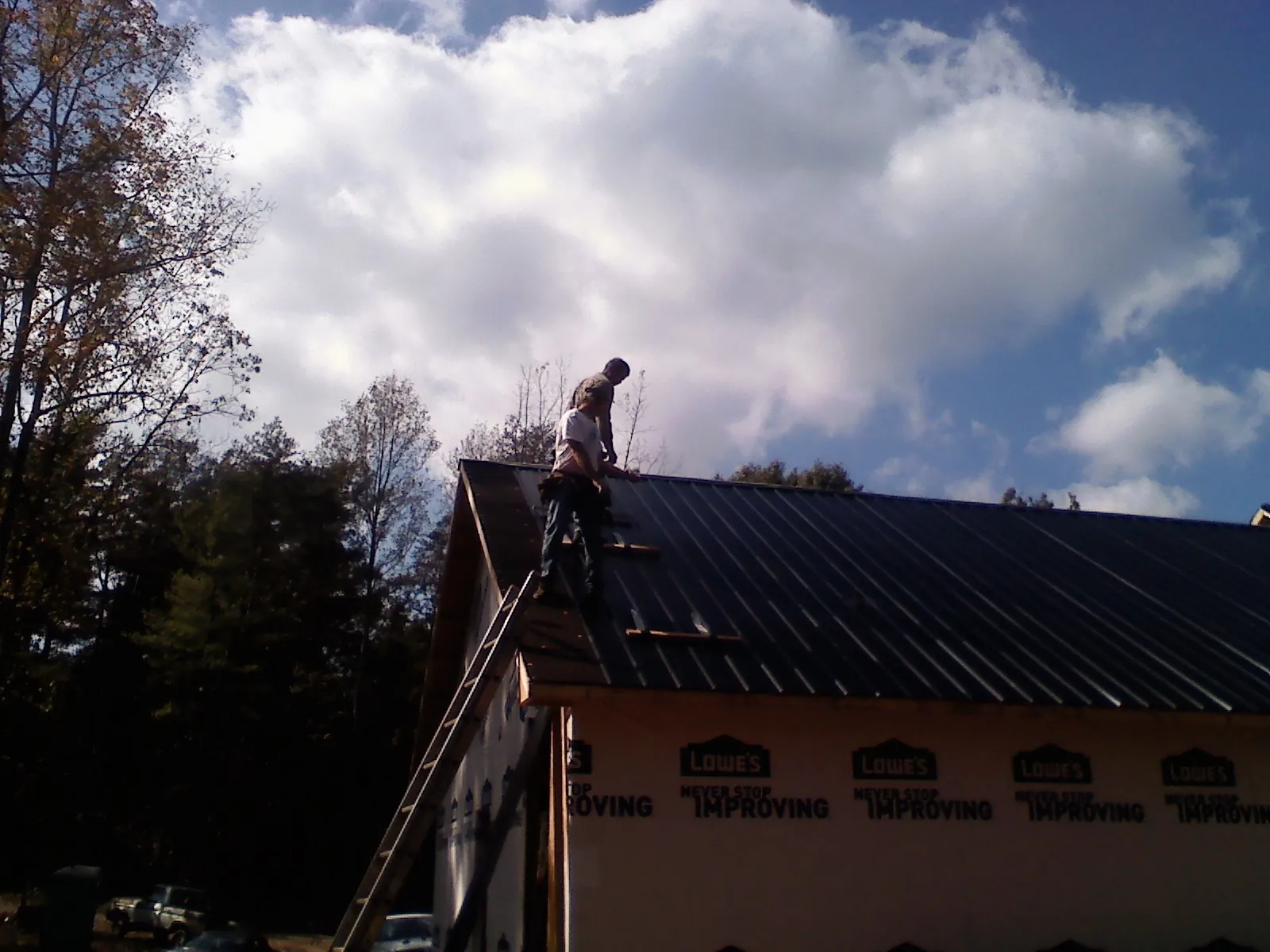 Roofer fastening dark metal panels high against a cloudy sky, from a Roof Inspection job in Robbins